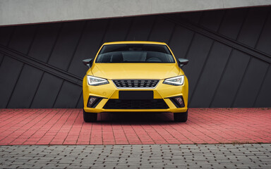 Yellow car on a city street. Front view of compact taxi-colored vehicle in parking lot with cobbled floor.