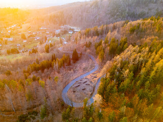 A winding road cuts through a forest of trees in autumn hues during sunset. The vibrant colors...