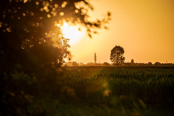 Golden sunset over italian countryside with bell tower and cultivated fields