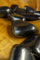 Collection of black stones on a wooden surface. The stones are arranged in a line, with some...