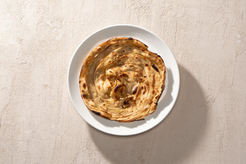 Kerala porotta or paratha on a white plate with a textured background