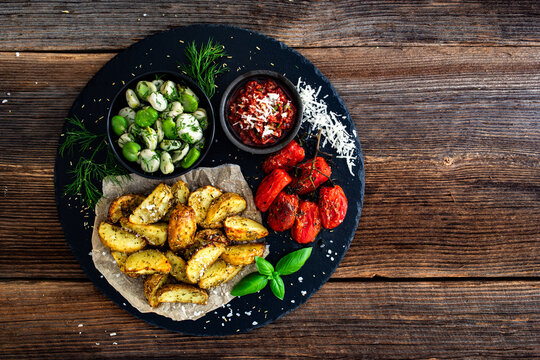 Boiled broad bean with roasted potatoes and cherry tomatoes with tomato pesto on wooden table