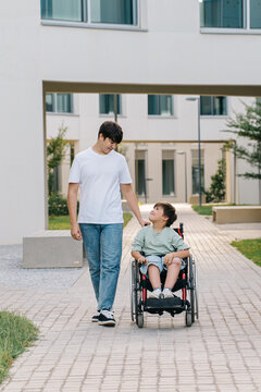 A teenager with his sma brother in a wheelchair walking down the street