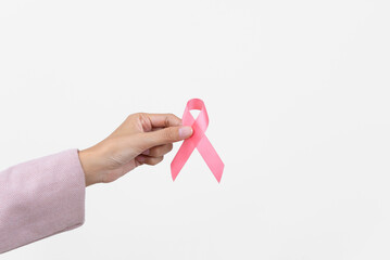 Close up asian woman breast cancer patient putting pink ribbon on hand as symbol of breast cancer...