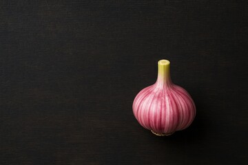 Close-up of a pink garlic bulb on a dark chopping board, showcasing its vibrant color and distinct aroma.