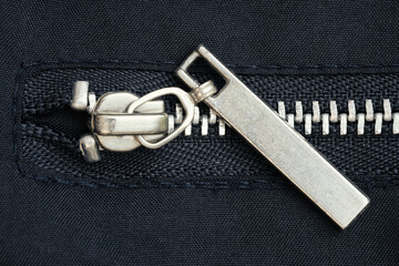 Close-up of metallic zipper slider on dark fabric background showing texture and detail