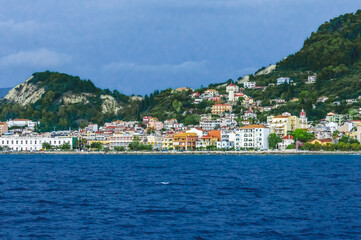 Obraz premium Seaside view of colorful coastal town with red-domed churches and green hills in Zakynthos island, Greece, seen from the water.