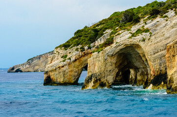 Natural rocky sea arches and colorful cliff formations at the famous Blue Caves in Zakynthos island, Greece, on a calm blue Mediterranean day.