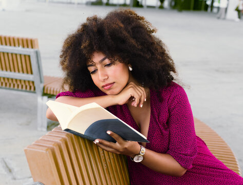 Woman reading on a bench wearing a pink dress