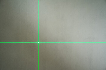 The green laser line from the leveling device shows the crossing of vertical and horizontal lines on the concrete wall.