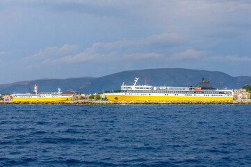 Two bright yellow passenger ferries docked at a Greek island port, with scenic town buildings and...