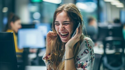 A young woman laughing while talking on the phone in an office is useful for topics related to work environment and communication.