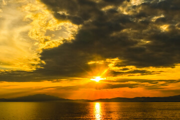 Golden sunset over the Aegean Sea during ferry trip from Keramoti to Thassos, with dramatic clouds and glowing reflections on the water.

