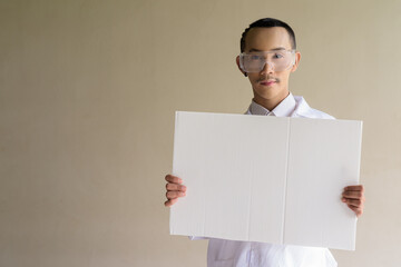 Portrait of a young scientist gay man wearing safety glass goggles and holding blank board with...
