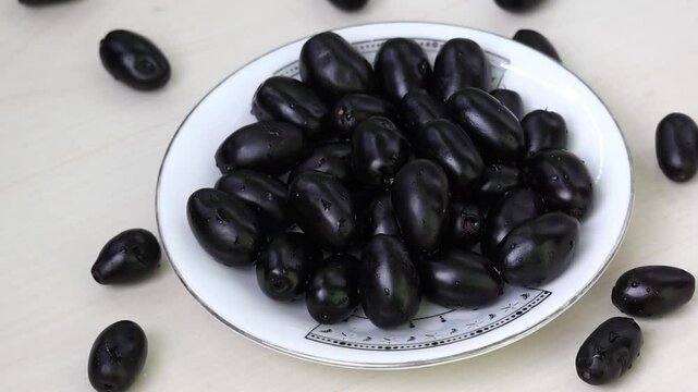 Fresh Black Plums on white plate, also known as Jamun, Java Plum, Malabar Plum, Jambolan. Syzygium cumini fruit, perfect for healthy eating and natural produce visuals.