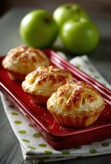 Freshly Baked Apple Pies on Red Plate with Green Apples in Background, Rustic Kitchen Setting with Natural Lighting and Delicious Pastry Texture