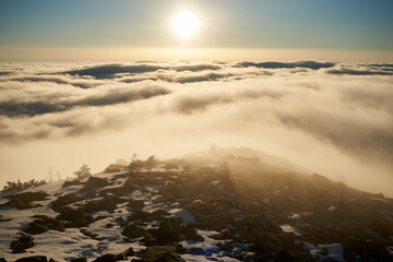 Sunrise over snow-covered mountain peak. Warm golden light of rising sun bathes clouds in soft hues...