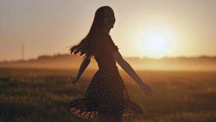Happy young woman spinning in a field at sunset, enjoying the golden hour light and the peace of...