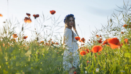Slavic woman with blue flower crown strolling through vibrant poppy field on sunny summer day