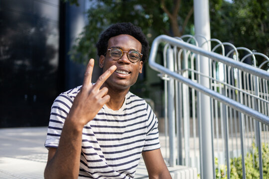 Student sitting outdoors with peace sign gesture