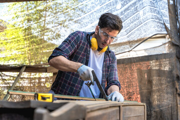 Carpenter man using manual hand saw cutting wood working in carpentry workshop