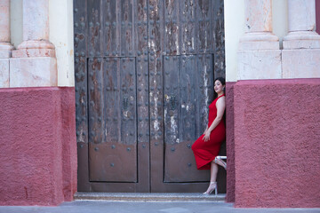 Young, beautiful, brunette woman in a nice red party dress and heels, leaning against the frame of...