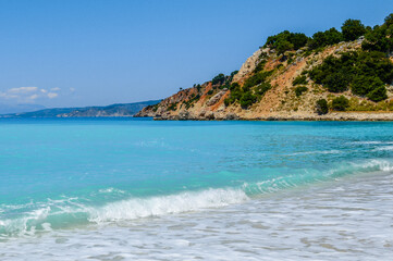 Gentle wave and turquoise water at Agia Kyriaki beach near Zola, Kefalonia, Greece, with red rocky...