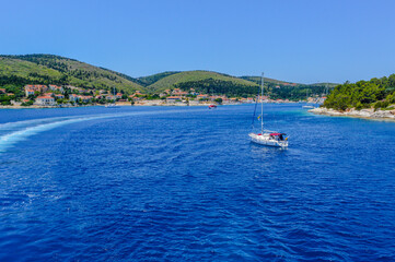 Ferry entering Fiskardo bay in Kefalonia, Greece, with a sailing boat on vivid blue waters,...
