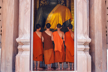 young buddhist novice monks, seen from behind, looking at big buddha statue in golden sash in Wat Chedi Luang temple, Chiang Mai, Thailand.	
