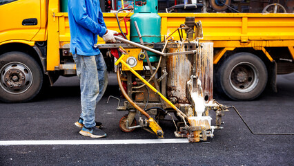 A worker operates a specialized road marking machine, laying a fresh white line on asphalt. Essential infrastructure maintenance highlights urban development and precision.

