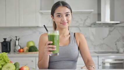 A woman smiling at a juice in her hand, kitchen background