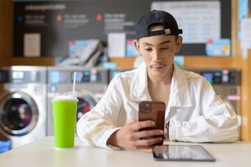 Non binary gay man in laundry shop using mobile phone
