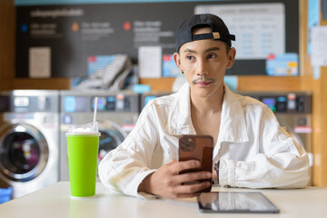 Non binary gay man in laundry shop using mobile phone