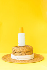 Summer Travel Essentials – Sunscreen Bottle with Straw Hat on Yellow Background