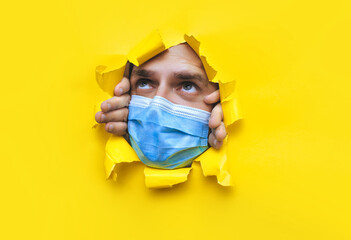 A man in a protective medical mask covering his nose and mouth looks into a broken hole in yellow...