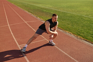 Athletic man stretching legs on running track at stadium