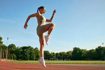 Athletic woman doing high knees workout on track at sunrise