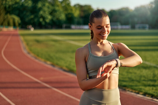 Smiling sporty woman checking fitness tracker on track