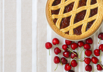 Cherry pie with a lattice crust and fresh cherries on a striped tablecloth, copy space