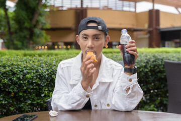 Non binary gay man eating burger outdoors during summer and drinking cola soft drink