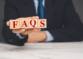 Businessman holding wooden blocks with red FAQs text, concept of help, support, or information.