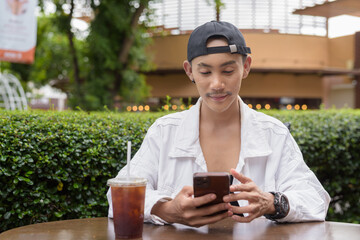 Non binary gay man drinking iced coffee in outdoors cafe restaurant and using mobile phone