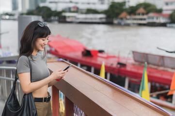 Happy young southeast asian woman teenager blogger explorer using smartphone searching tourism...