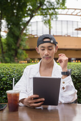 Non binary gay man drinking iced coffee in outdoors cafe restaurant and using tablet computer