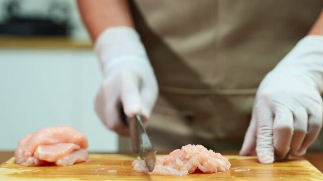 Closeup of gloved hands mincing raw chicken on wooden board, showcasing food preparation, kitchen hygiene, clean cooking