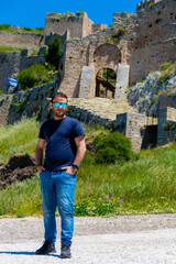 Man posing confidently in front of the medieval gate of Acrocorinth fortress in Corinth, Greece,...