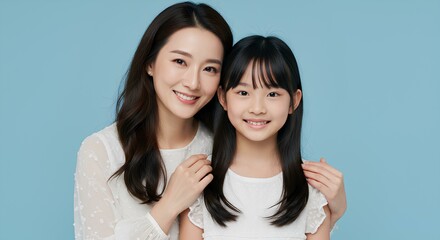 A smiling mother and daughter pose closely together in white outfits against a blue background.