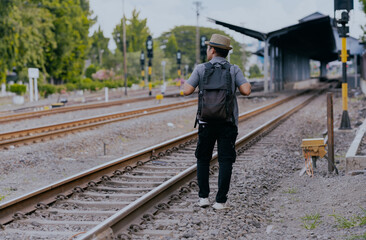 Asian man traveler with backpack in the railway. Traveler man wearing hat walking on the train...