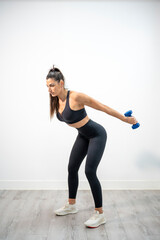 Woman doing tricep kickbacks using dumbbells with arms extended backward and leaning forward
