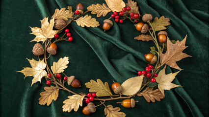 Beautiful autumnal wreath made of acorns, red berries, oak leaves, and pine cones lies on a dark background, creating a warm and festive atmosphere perfect for thanksgiving or fall celebrations
